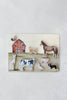 The Farm Animals Wooden Puzzle: A Tabitha Paige Puzzle showcases a red barn scene with a variety of farm animals—including a cow, horse, pig, sheep, dog, rooster, duck, and llama—set on a light background, making it an ideal educational toy for toddlers to learn about their favorite animals.