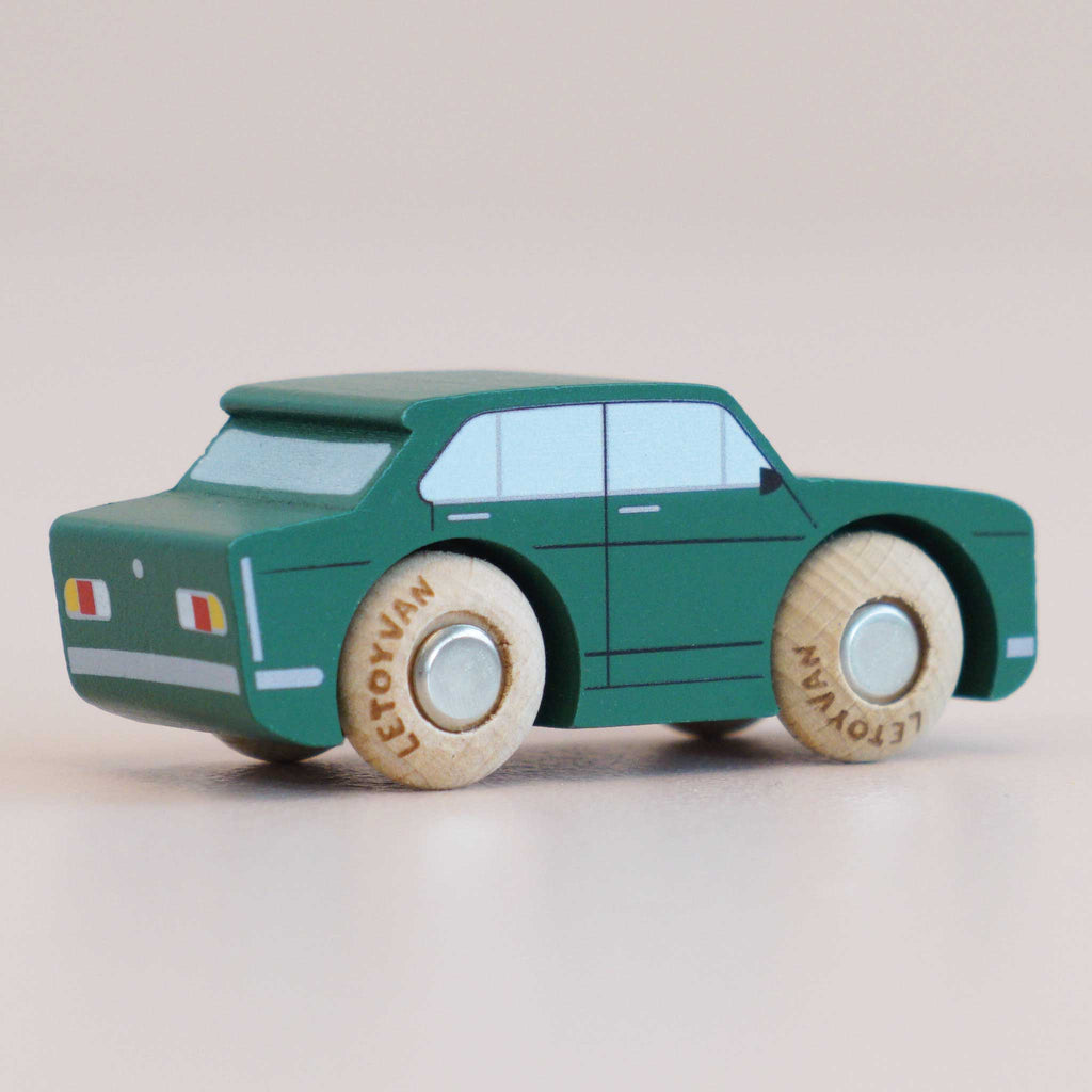 A No. 3 GT20 Tommy, a small green retro wooden car with painted windows and round natural wood wheels, made in England, is shown on a light surface.