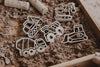 Plastic construction vehicle molds rest on brown kinetic sand in a wooden tray, accompanied by pieces of chalk. Ideal for sensory play, these molds feature a dump truck, cement mixer, backhoe, and other vehicles—making them the perfect companions to the Construction Cutter Set - Eco Playdough Tool.