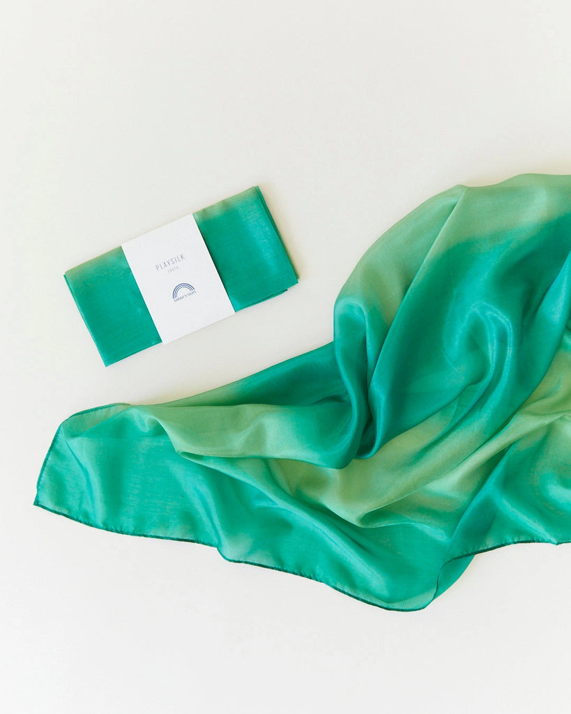 A vibrant green Sarah's Silk Earth Playsilk - Forest gracefully draped next to a business card with the text "patience" on a subtle off-white background.