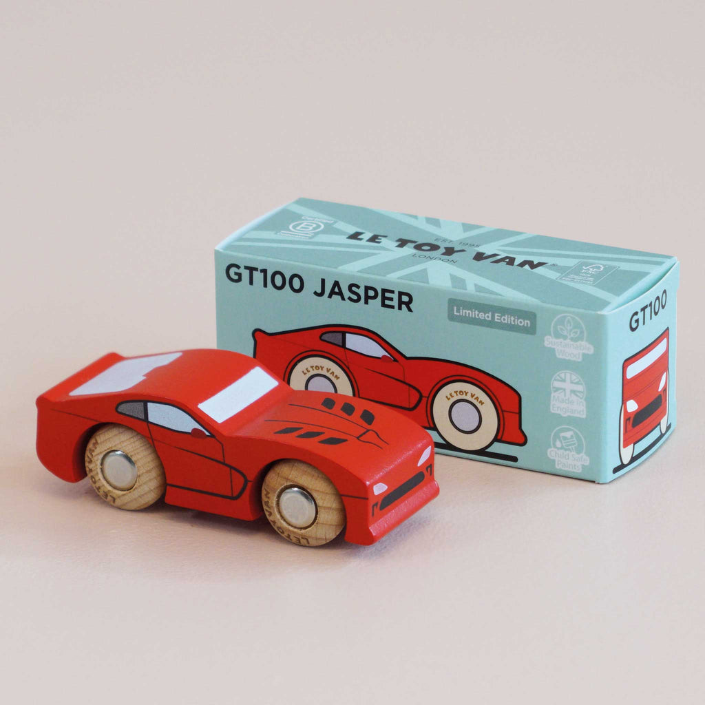 A red wooden sports car with light brown wheels, expertly crafted from sustainable wood, is displayed in front of a blue box labeled “No. 18 GT100 Jasper | Made in England” and adorned with an illustration of the same car, evoking classic performance motoring.