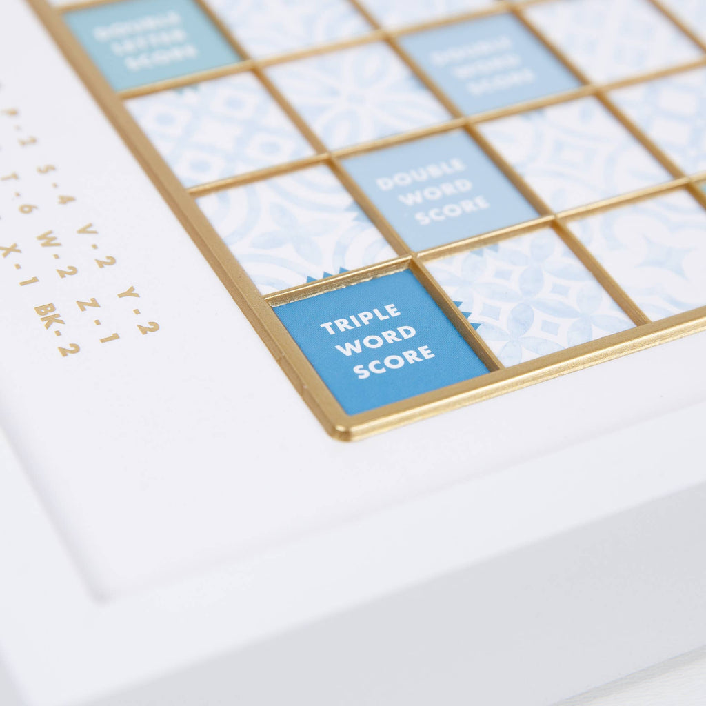 Close-up of a Scrabble Bianco Edition game board with a blue and white patterned grid, gold edges, and labeled squares including “Double Word Score” and “Triple Word Score.”
