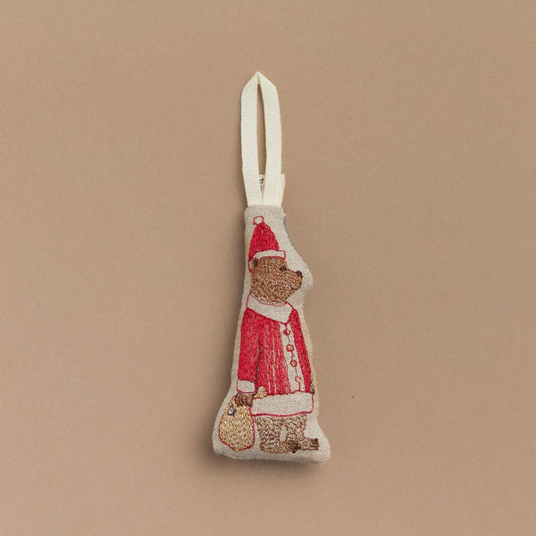 Introducing the Santa Bear Ornament: a delightful fabric bear dressed in a festive red suit, holding a small bag of presents. It comes with a white hanging loop at the top, ideal for bringing holiday cheer to any beige background.