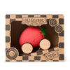 Sweetie The Strawberry Baby Car is an eco-friendly, red strawberry-shaped toy with green leaves and wooden wheels. Made from natural rubber, it comes in a brown "Oli & Carol Green Cars" box labeled for babies 0+.