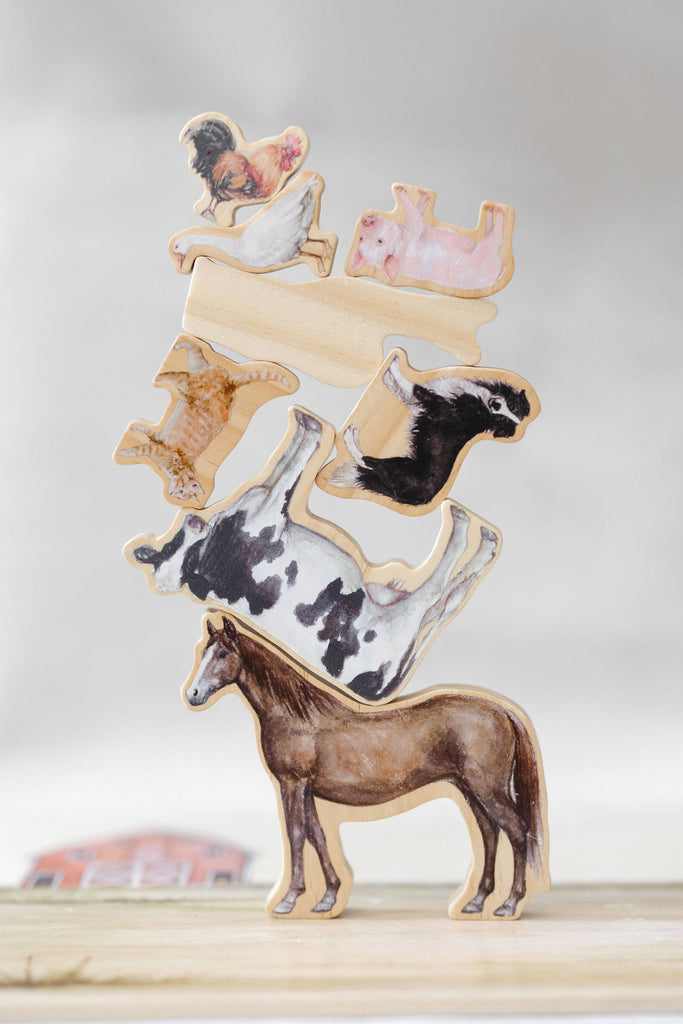Farm Animals Wooden Puzzle: A Tabitha Paige Puzzle features charming wooden animal figures—including a horse, cow, pig, cat, and chicken—stacked to form a balancing tower on a wooden surface with a plain background. This delightful toddler educational toy is perfect for encouraging fine motor skills and imaginative play.