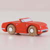 The No. 13 GT75 Marc, made in England, is a classic small wooden convertible car painted in racing red with white accents and natural wooden wheels, pictured on a light pink surface.