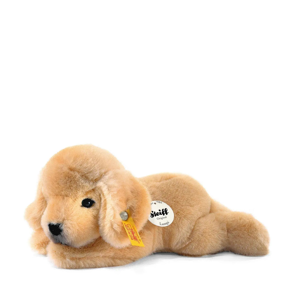 A Steiff, Golden Retriever Dog Stuffed Animal lying down, with distinctive Button in Ear trademark tags attached to its ear and side, against a white background.