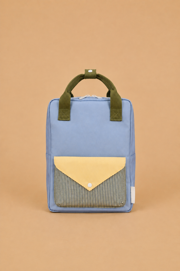 A Sticky Lemon Backpack Medium | Envelope | Cloud Blue, featuring a rectangular shape in blue with green handles and a yellow plaid-patterned flap pocket, crafted with a waterproof lining made from recycled PET bottles, is displayed against a plain tan background.