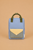 A Sticky Lemon Backpack Medium | Envelope | Cloud Blue, featuring a rectangular shape in blue with green handles and a yellow plaid-patterned flap pocket, crafted with a waterproof lining made from recycled PET bottles, is displayed against a plain tan background.