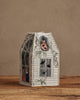 The Coral & Tusk Haunted House Tissue Box Cover, featuring jack-o’-lanterns, bats, and cobweb embroidery, sits on a wooden surface against a plain beige background.