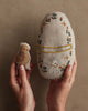 Two hands hold a small yellow chick and the Coral & Tusk Pocket Easter Egg—an oval pillow with floral patterns and a rabbit—against a beige background, making them perfect Easter basket additions.