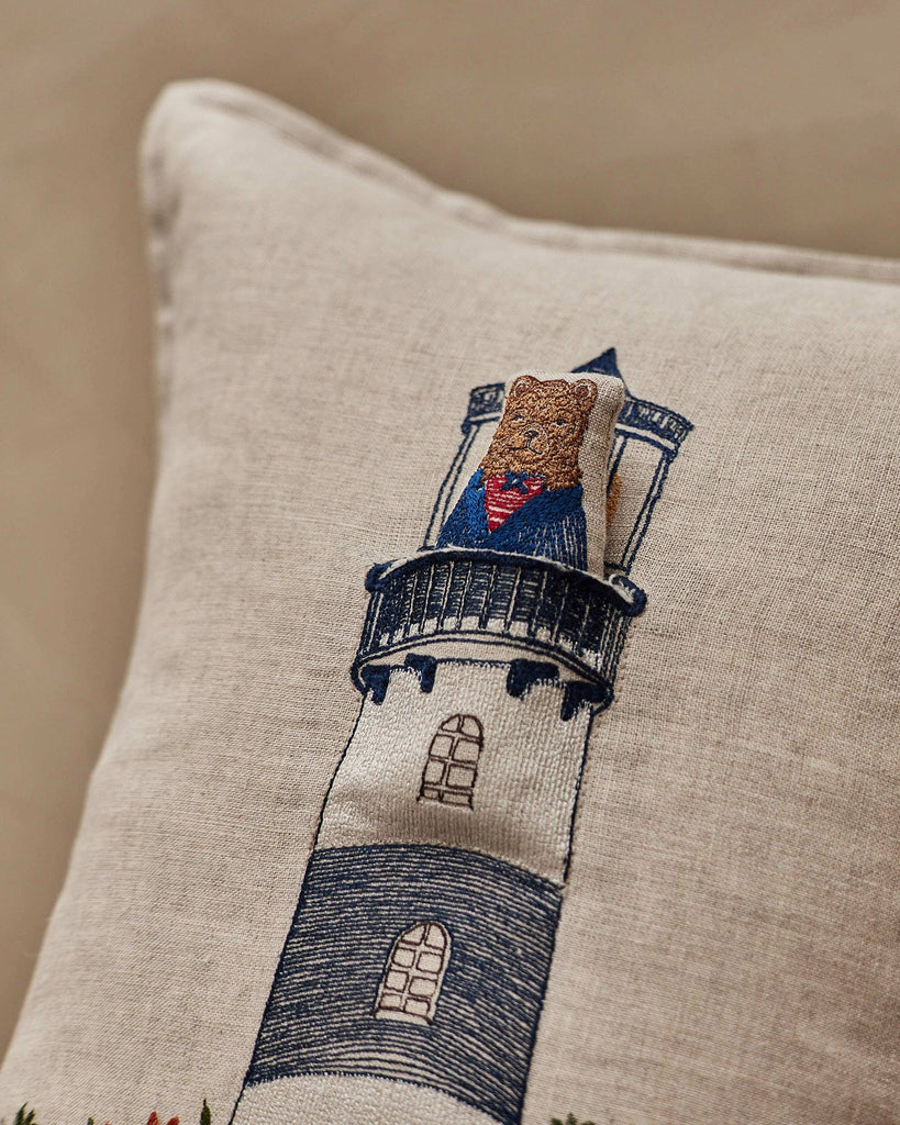 The Coral & Tusk Lighthouse Friends Pocket Pillow features an embroidered bear cookie dressed as Superman sitting on a lighthouse—perfect for adding playful nautical charm to your home décor.