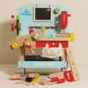 The Wooden Tool Bench is a colorful pretend playset with toy tools—hammer, saw, screwdriver, ruler, nuts, bolts—and a canvas bag labeled “My First Toolbench.” The bench features the “Le Toy Van” brand.