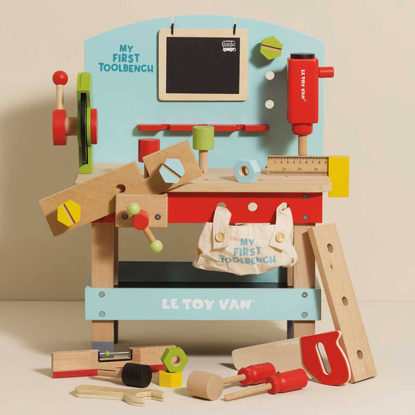 The Wooden Tool Bench is a colorful pretend playset with toy tools—hammer, saw, screwdriver, ruler, nuts, bolts—and a canvas bag labeled “My First Toolbench.” The bench features the “Le Toy Van” brand.