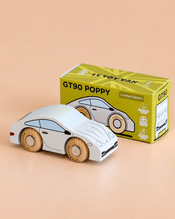 A white wooden sports car with beige wheels is displayed beside a yellow and green box labeled “No. 16 GT90 Poppy | Made in England” and “Limited Edition” on a light beige surface, highlighting the charm of this timeless toy.