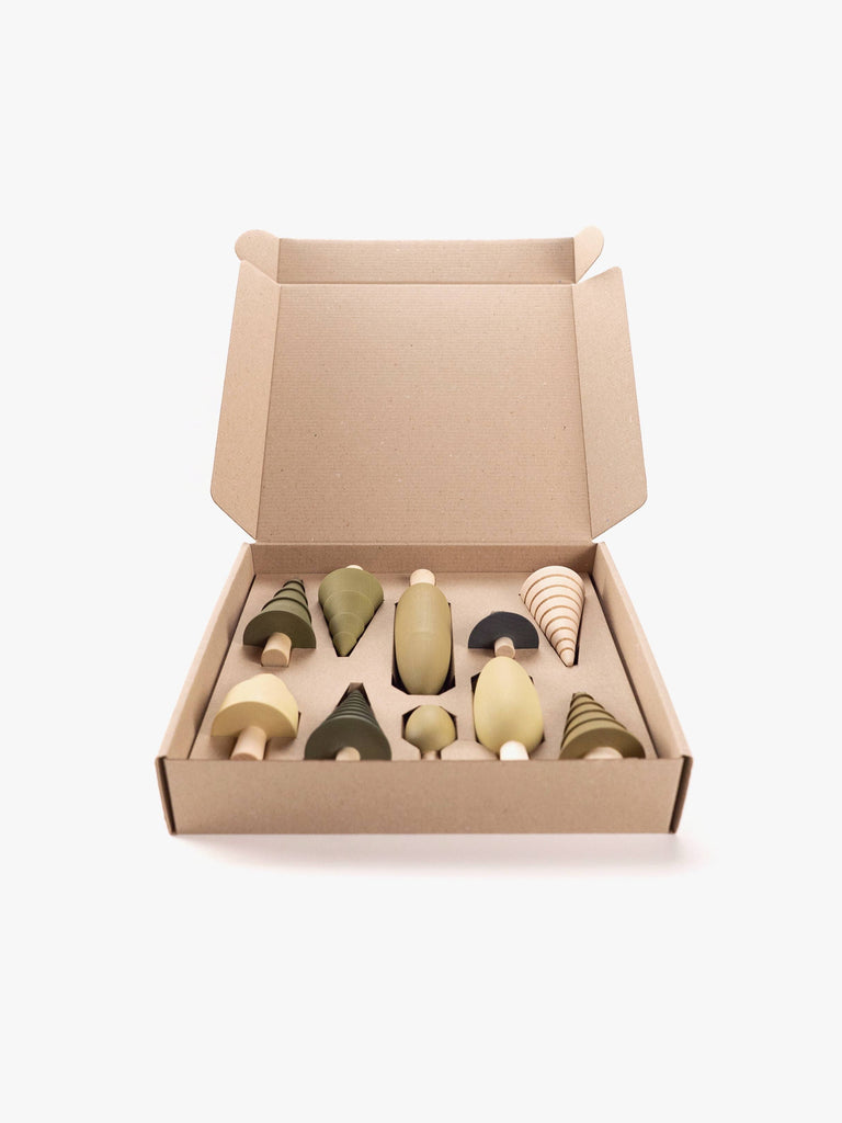 An open cardboard box reveals a delightful collection of Wooden Forest Set toys—small, wooden trees in diverse shapes and soothing shades of green and beige. Set against a plain white background, these imaginative play toys inspire creativity and exploration.