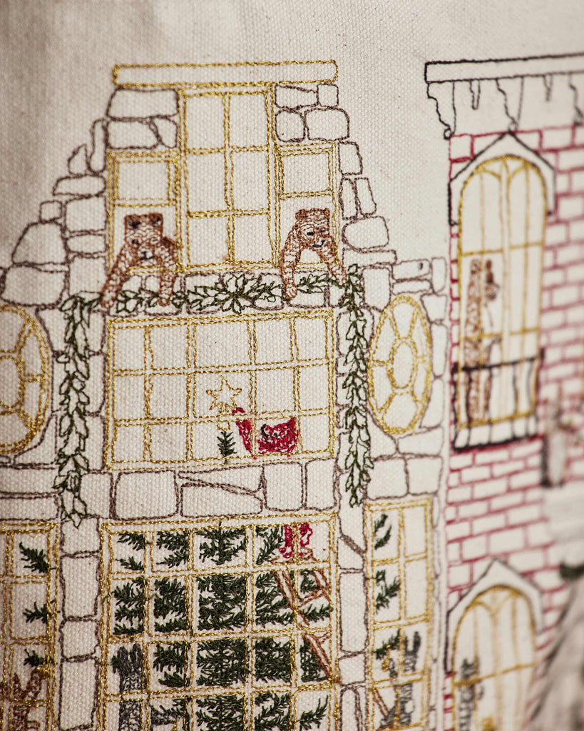 Featuring detailed embroidery of windows, greenery, a Christmas tree, and festive touches in gold, green, red, and brown thread—perfect as a decorative accent for your Home for the Holidays Bucket.