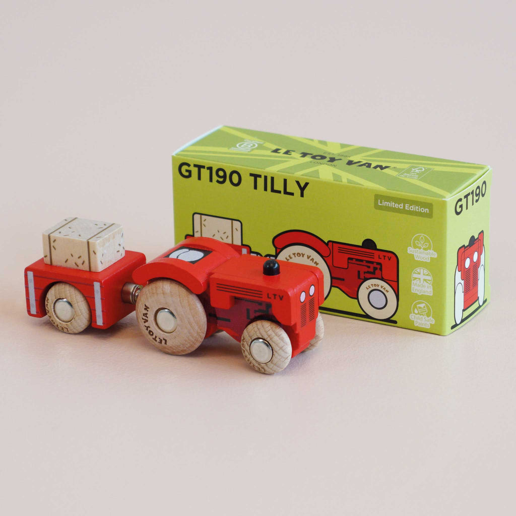 A vintage wooden tractor, painted red and featuring a trailer with block, is displayed next to a green box labeled “No. 34 GT190 Tilly | Made in England.” This delightful farmyard toy sparks the imagination of both children and collectors.