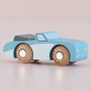 The No. 1 GT10 Justin | Made in England is a small blue and white wooden car with wooden wheels and a black rear spoiler, displayed on a light pink surface—a charming keepsake for any collection.