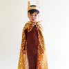 A young child wears a brown costume, headband with deer ears, and the Sarah's Silks Animal Print Playsilk - Fawn as a cape, standing against a plain white background.