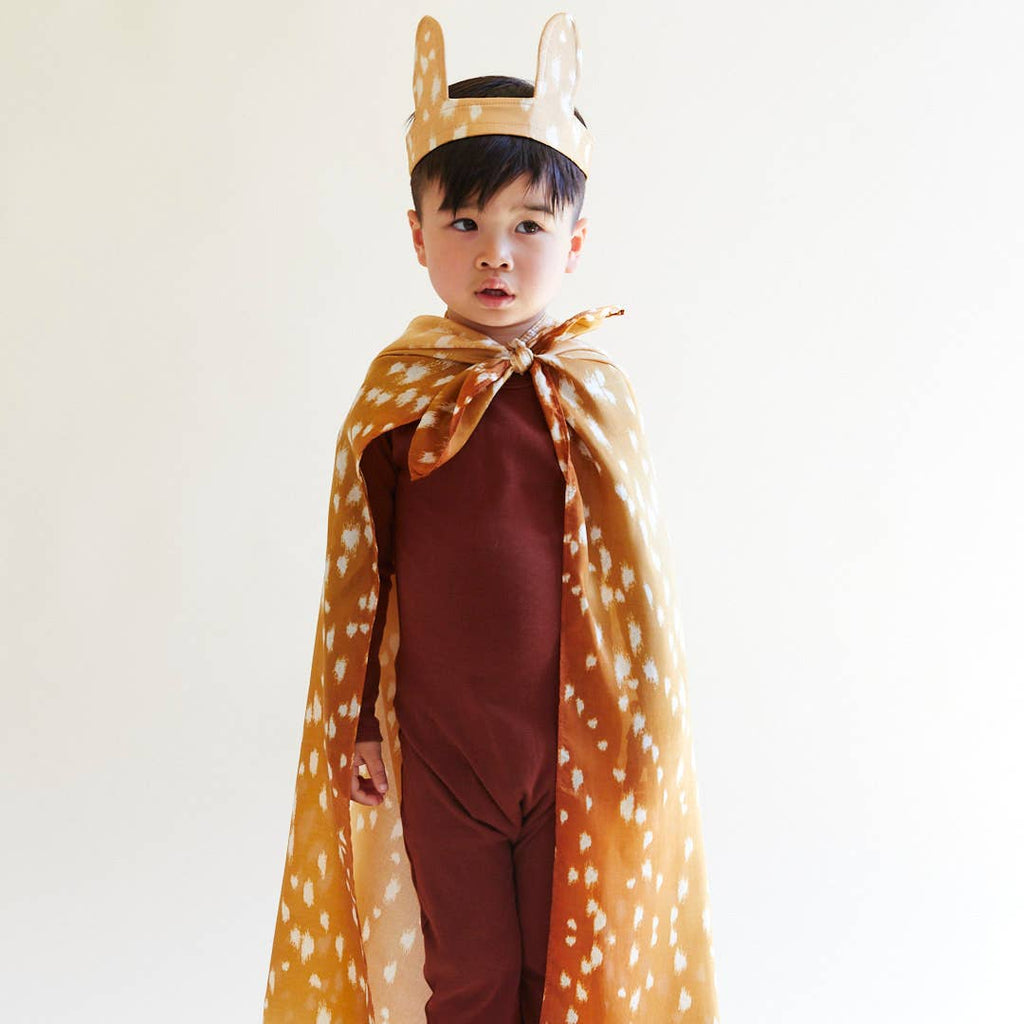 A young child wears a brown costume, headband with deer ears, and the Sarah's Silks Animal Print Playsilk - Fawn as a cape, standing against a plain white background.