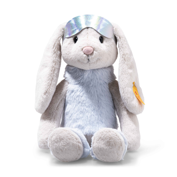 Steiff Hoppie Rabbit in Ski Outfit, 12 inches, sits upright with long floppy ears, soft light grey fur, and a light blue body. It wears a shiny silver sleep mask and a yellow tag on its left ear against a white background.