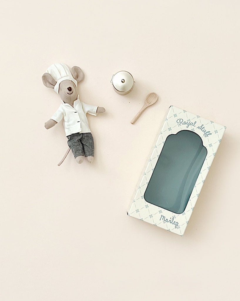 A Maileg Little Chef's Kitchen scene features a mouse beside a wooden spoon, metal pot, and empty “Royal Staff” toy box on a light beige background.