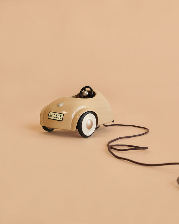 The Maileg Car, Mouse - Wheat is a small beige toy car with a steering wheel and white wheels, attached to a brown pull string, displayed against a plain beige background.
