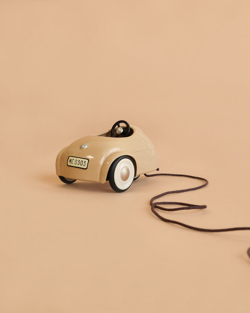 The Maileg Car, Mouse - Wheat is a small beige toy car with a steering wheel and white wheels, attached to a brown pull string, displayed against a plain beige background.