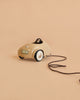 The Maileg Little Brother Adventure Set features a small beige car with a black steering wheel and white wheels, attached to a long black pull string, displayed on a plain beige background.