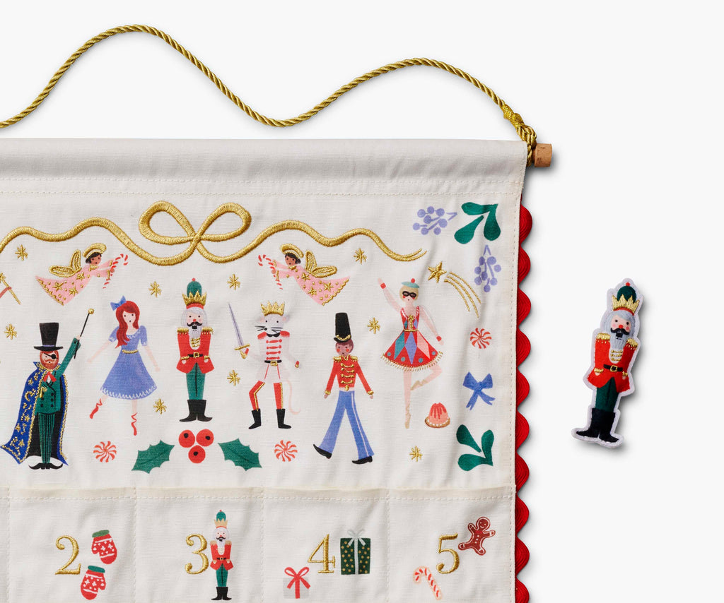 Nutcracker Embroidered Hanging Advent Calendar - Red featuring embroidered nutcracker characters and holiday motifs, with a separate nutcracker figurine to place in the numbered pockets.