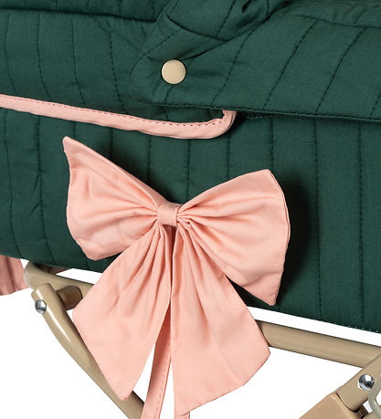 Close-up of the Doll Pram - Bowie Smoke Pine, showcasing a quilted fabric item in green made from organic cotton and adorned with a pink fabric bow. The pram, embodying a vintage style, features a stitched pattern and brass button accents, all gracefully supported by a beige metal frame.