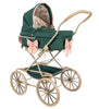 The Doll Pram - Bowie Smoke Pine is a vintage-style stroller that combines recycled materials and craftsmanship with dark green quilted fabric and a robust wooden frame. It features large wheels, pink bow accents, and a canopy adorned with a horse pattern, capturing the elegance of classic posh vintage design.