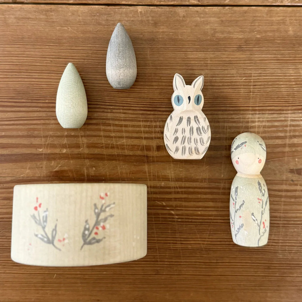 Five wooden toys from the Hello Winter Set (Grapat X Ostheimer Limited Edition)—two teardrops, an owl, a berry box, and a peg doll—are arranged on a wooden surface.