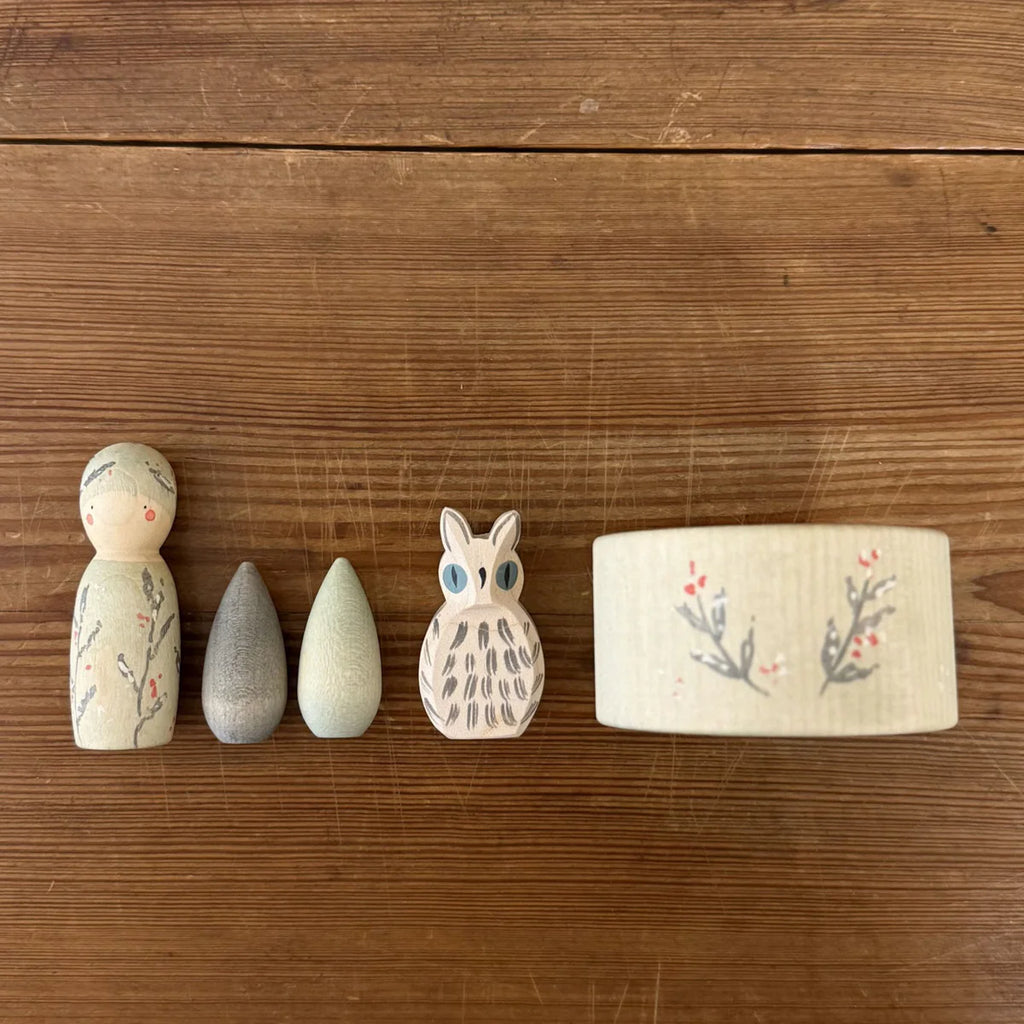The Hello Winter Set (Grapat X Ostheimer Limited Edition) features five painted wooden toys—a figure, two teardrops, an owl, and a round container—adorned with floral or leaf motifs on a wooden surface.