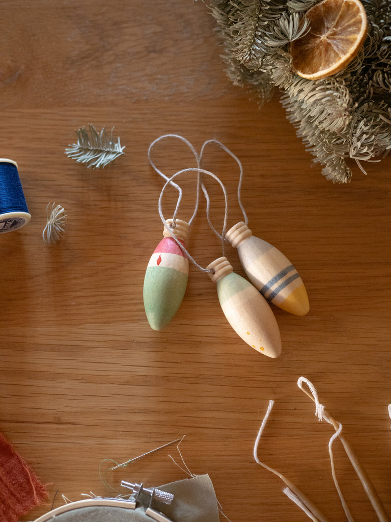 The Grapat Ornament Set - Winter Sparkles features three hand-painted ornaments with string loops, displayed on wood beside dried greenery, an orange slice, and blue thread—festive accents for enchanting home decor.