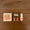 The Hello Autumn Set (Grapat X Ostheimer Limited Edition) features a square block with leaf design, elastic band, small hedgehog, two mushroom-shaped pieces, and a painted peg doll with orange leaf pattern on a wooden surface.