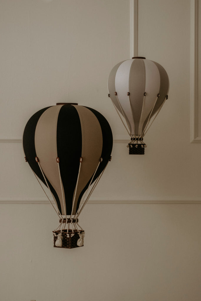 The Hot Air Balloon - Black, a decorative wooden model, hangs beautifully against a beige wall—an ideal handmade accent for children's room decor or as charming black balloon wall art.