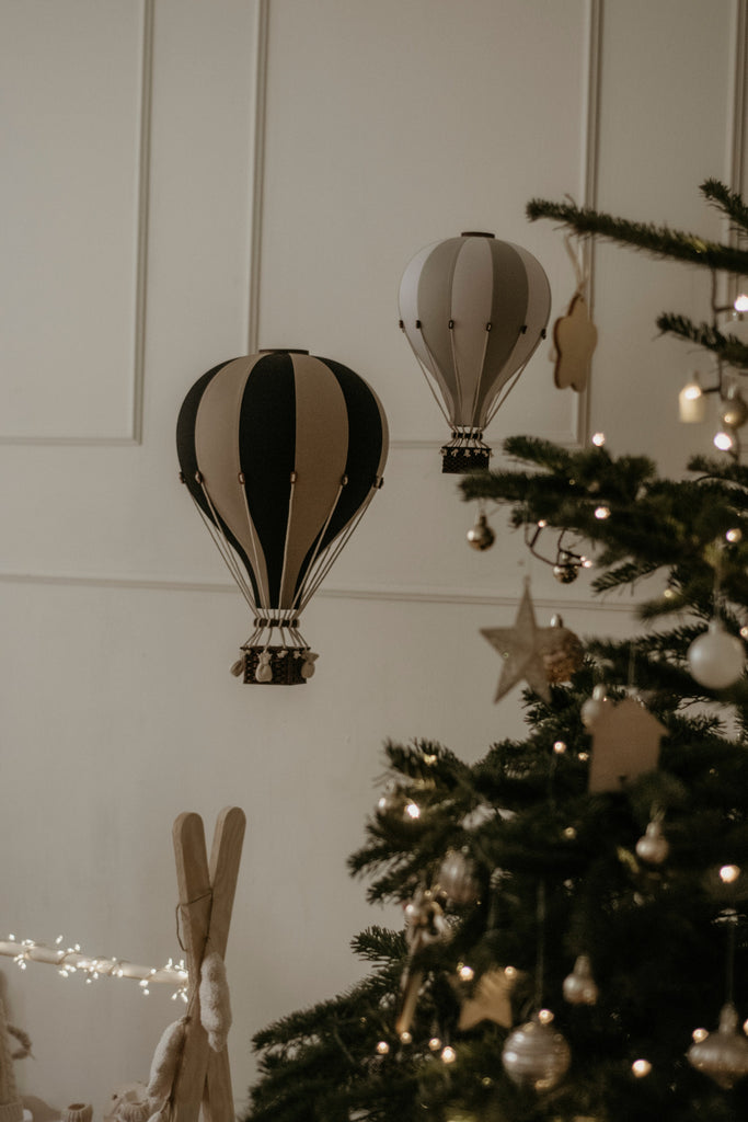 Two decorative Hot Air Balloon - Black ornaments hang on a white wall beside a Christmas tree with lights and ornaments, creating a cozy, festive atmosphere with warm lighting—perfect for decorating children's rooms.