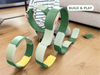 A child plays on a wooden floor, constructing looping structures with green and white curved pieces from the WaytoPlay: Arches - Creator Set, an eco-friendly recycled plastic toy. A “BUILD & PLAY” label appears in the top right corner.
