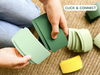 Hands holding green plastic cards—components from the WaytoPlay: Arches - Creator Set—over a textured carpet, with more cards from the set scattered nearby. The words “CLICK & CONNECT” appear in a rounded rectangle at the top right of the image.