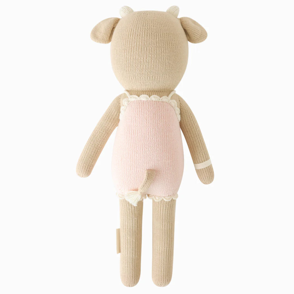 Cuddle + Kind Ava the Cow - Powder Pink is a hand-knit Peruvian doll made from 100% cotton yarn, featuring a cow with beige limbs, horns, and ears, dressed in light pink with a small tail showing from the back.