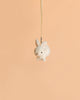 The Bukowski - Zeus Bunny Bag Charm, a small white plush bunny keychain, is suspended by a ribbon against a plain peach-colored background.