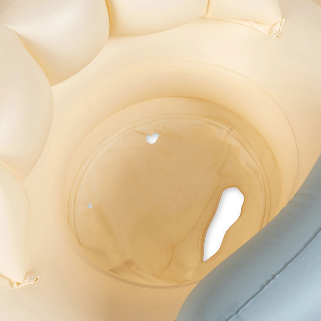 Close-up view of an Inflatable Baby Swim Ring - Car, resembling an inflatable swim ring, with a circular opening in the center and a grey edge on the right side. The interior appears cushioned with a soft, textured material. Two small white patches are visible inside the opening. Made from durable PVC.