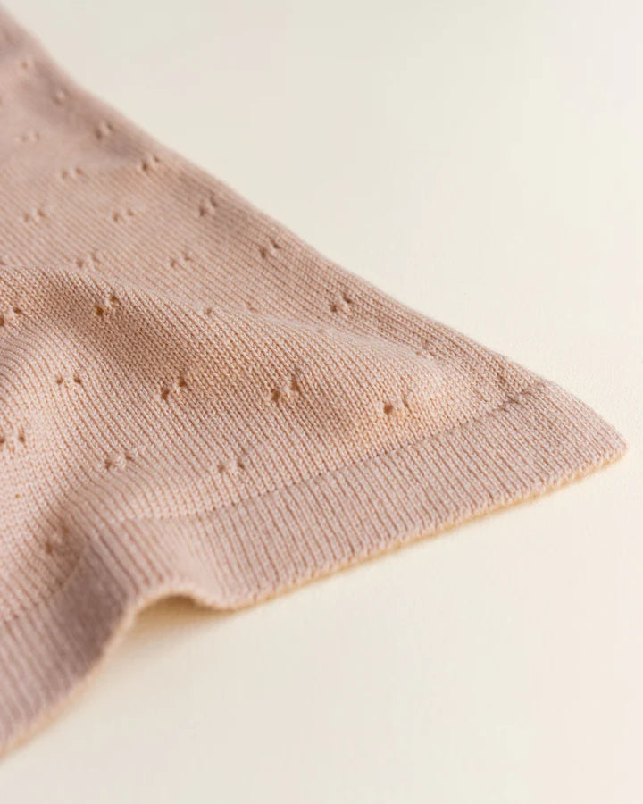 Close-up of a apricot handmade merino wool Bibi blanket with a textured, dotted pattern, draped gracefully with a soft focus on a light background.