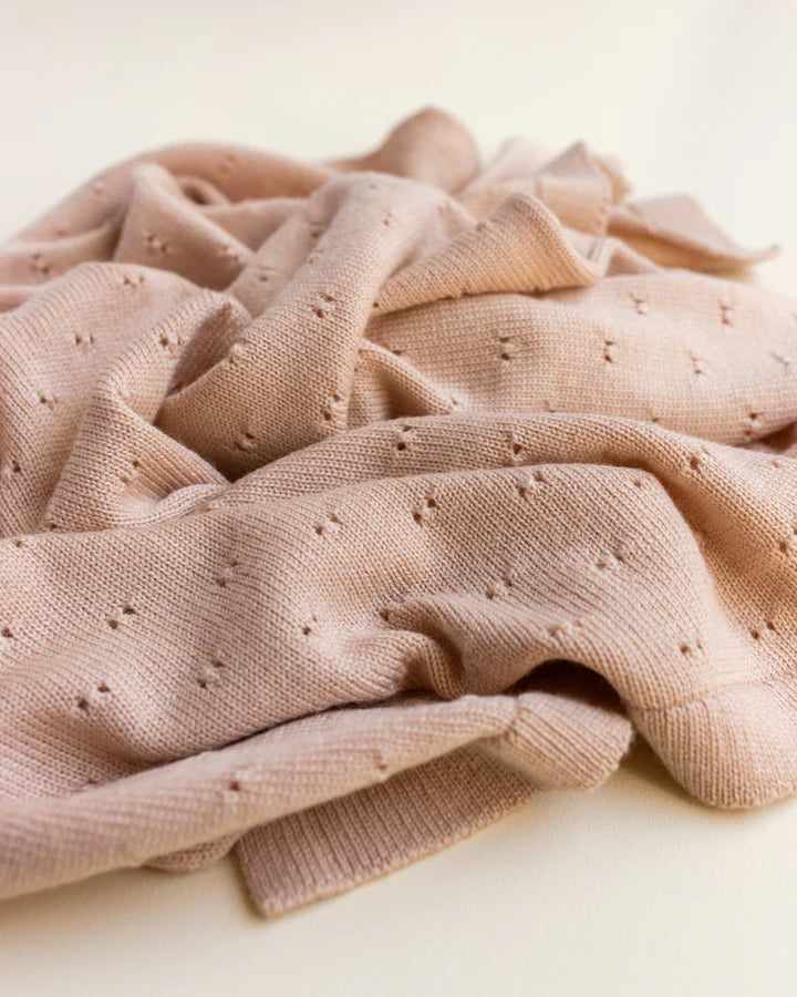 Close-up image of a textured, light pink Handmade Merino Wool Bibi Blanket - Apricot with delicate, small perforations spread throughout, resting softly on a plain surface.
