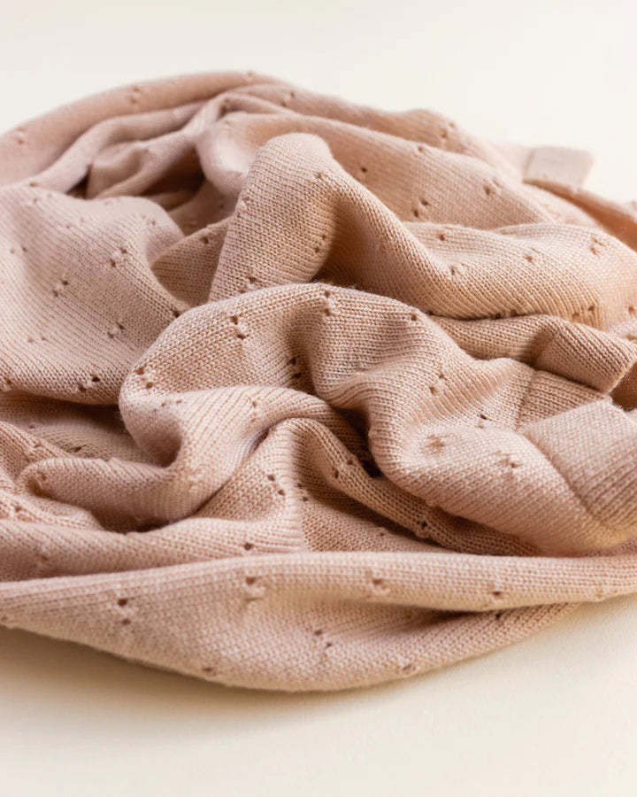 A crumpled apricot Handmade Merino Wool Bibi Blanket with a delicate, perforated pattern, creating a textured appearance on a plain background.
