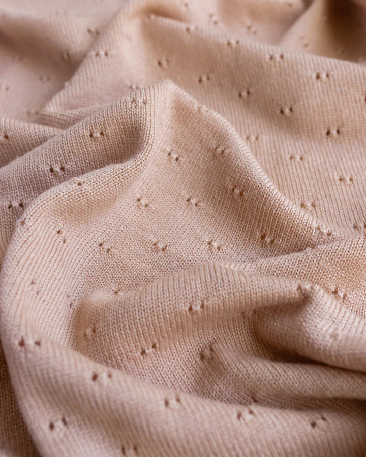 Close-up of a textured beige Handmade Merino Wool Bibi Blanket - Apricot with tiny, evenly spaced embroidered dots, creating a subtle, elegant pattern on the soft, wrinkled material.