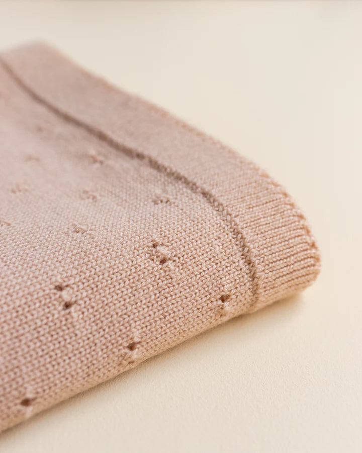 Close-up of a folded Handmade Merino Wool Bibi Blanket - Apricot with a textured knit pattern, showing delicate details on a soft beige background.
