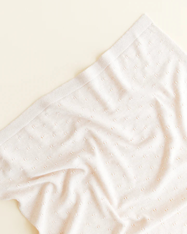 Sentence with product name: A close-up image of a handmade Merino Wool Bibi Blanket in cream color with tiny, ornamental dots on a light beige background. This showcases a detail of the blanket's design and texture.